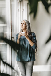 Frau mit Schüssel Kaffee schaut durch das Fenster - KNSF000337