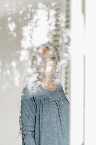 Frau hinter spiegelnder Fensterscheibe stehend, lizenzfreies Stockfoto