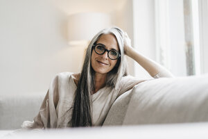 Porträt einer lächelnden Frau mit langen grauen Haaren, die auf der Couch sitzt - KNSF000347