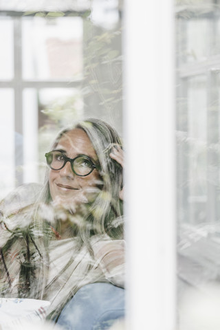 Portrait of smiling woman sitting in winter garten looking through window stock photo