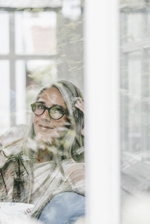 Porträt einer lächelnden Frau, die im Wintergarten sitzt und durch das Fenster schaut - KNSF000352