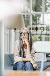 Pensive woman sitting in winter garden looking through window - KNSF000353