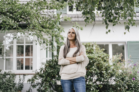 Lächelnde Frau mit langen grauen Haaren im Garten stehend, lizenzfreies Stockfoto