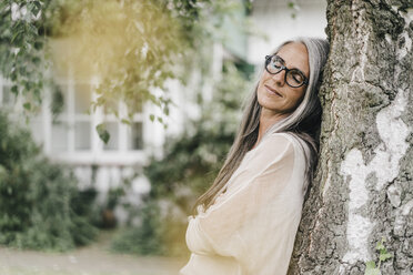 Portrait of woman with eyes closed leaning against tree trunk - KNSF000359