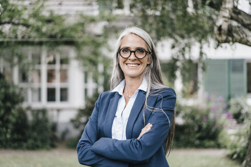 Portrait of smiling businesswoman wearing spectacles standing in the garden - KNSF000362