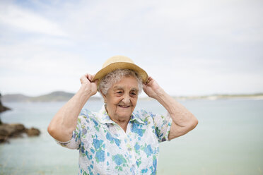 Portrait of smiling senior woman putting on straw hat - RAEF001413