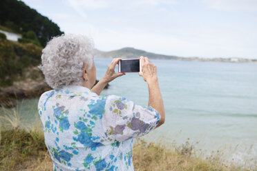 Rückansicht einer älteren Frau, die mit ihrem Smartphone ein Bild vom Meer macht - RAEF001417