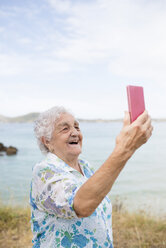 Glückliche ältere Frau nimmt Selfie am Strand - RAEF001418