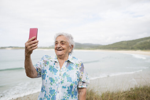 Happy senior woman taking selfie on the beach - RAEF001419