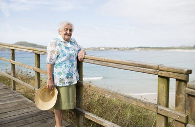 Glückliche ältere Frau an der Strandpromenade stehend - RAEF001420