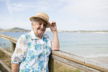 Glückliche ältere Frau mit Strohhut an der Strandpromenade stehend - RAEF001421