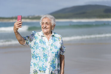 Lächelnde ältere Frau macht Selfie am Strand - RAEF001425