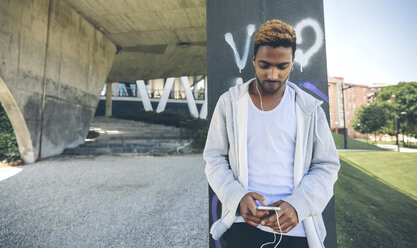 Young man listening music with earphones looking at smartphone - DAPF000276