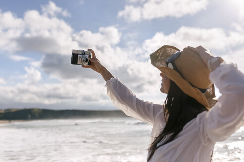 Asturien, Spanien, schöne junge Frau mit einer Kamera am Strand - MGOF002207