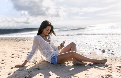 Spanien, Asturien, schöne junge Frau mit Smartphone am Strand - MGOF002209