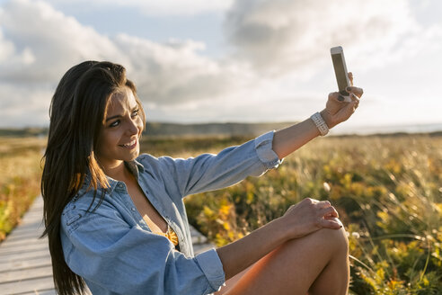 Spanien, Asturien, schöne junge Frau macht ein Selfie an der Strandpromenade - MGOF002224