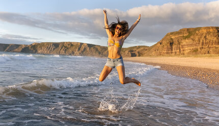 Spain, Asturias, beautiful young woman jumping on the beach - MGOF002232