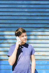 Young man standing in front of blue gate using smart phone - FMOF000118