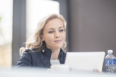 Blond woman in canteen reading messages on digital tablet - ZEF009780