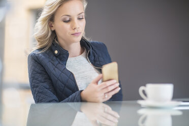 Blonde Frau in der Kantine liest Nachrichten auf dem Smartphone - ZEF009781