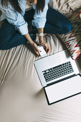 Junge Frau mit Smartphone und Laptop auf dem Bett - BOYF000566