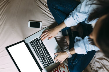 Young woman using smartphone and laptop on bed - BOYF000567