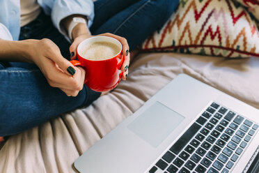 Young woman sitting on bed, coffee cup, laptop and smartphone - BOYF000574