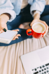 Junge Frau sitzt auf dem Bett, Kaffeetasse, Laptop und Smartphone - BOYF000575