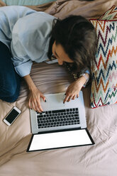 Young woman using laptop on bed, smartphone - BOYF000577