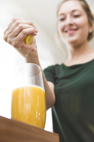 Frau drückt Zitronensaft in ein Glas mit selbstgemachtem Smoothie, lizenzfreies Stockfoto