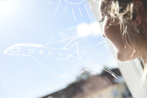 Woman looking at aeroplane drawn on windowpane - MIDF000785