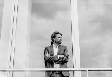 Businessman standing at glass front of a building - KNSF000380