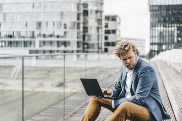 Businessman sitting on bridge using laptop - KNSF000388