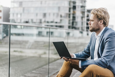 Businessman sitting on bridge using laptop - KNSF000391