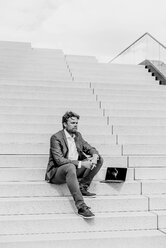 Businessman sitting on stairs with laptop - KNSF000396