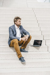 Businessman sitting on stairs with laptop - KNSF000398