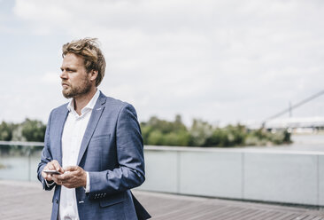 Businessman standing on bridge holding cell phone - KNSF000405