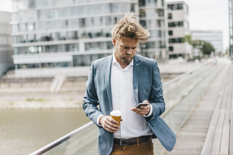 Geschäftsmann mit Handy und Kaffee zum Mitnehmen auf der Brücke, lizenzfreies Stockfoto