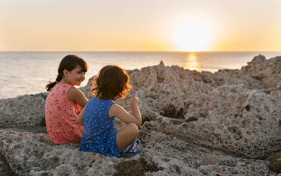 Spain, Gijon, group picture of three little girls sitting at rocky coast  stock photo