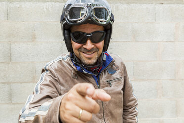 Lächelnder Motorradfahrer mit Sonnenbrille und Helm, der auf den Betrachter zeigt - JUNF000586