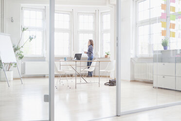 Frau steht am Fenster in einem hellen Büro - RBF004989