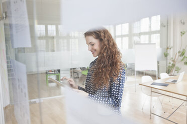 Woman in office using digital tablet behind glass pane - RBF004995