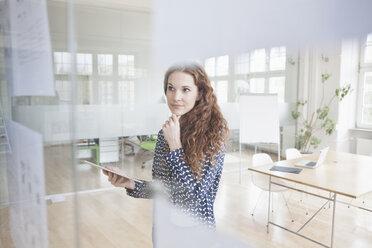 Frau im Büro schaut auf Papiere an der Glasscheibe - RBF004996