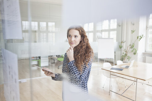 Frau im Büro schaut auf Papiere an der Glasscheibe - RBF004996