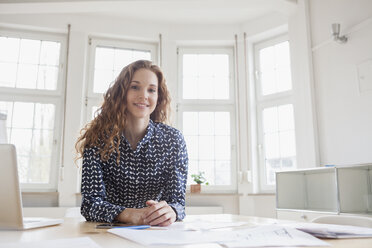 Porträt einer lächelnden Frau am Schreibtisch im Büro - RBF005003