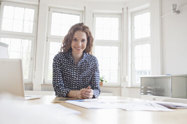 Porträt einer lächelnden Frau am Schreibtisch im Büro - RBF005004