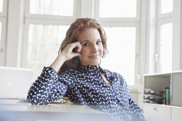 Portrait of smiling woman at desk in office - RBF005022