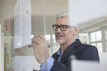 Geschäftsmann im Büro schreibt auf Papier an Glasscheibe - RBF005036