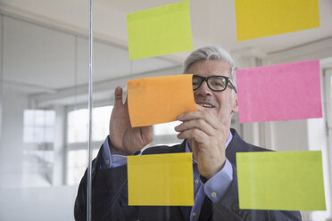 Businessman in office attaching adhesive notes at glass pane - RBF005037