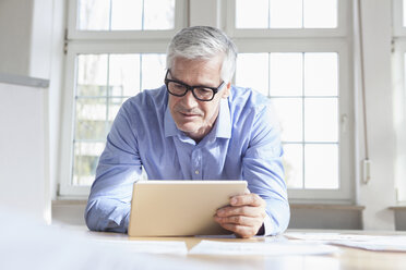 Älterer Geschäftsmann sitzt auf einem Stuhl im Büro und hält ein Tablet - RBF005050